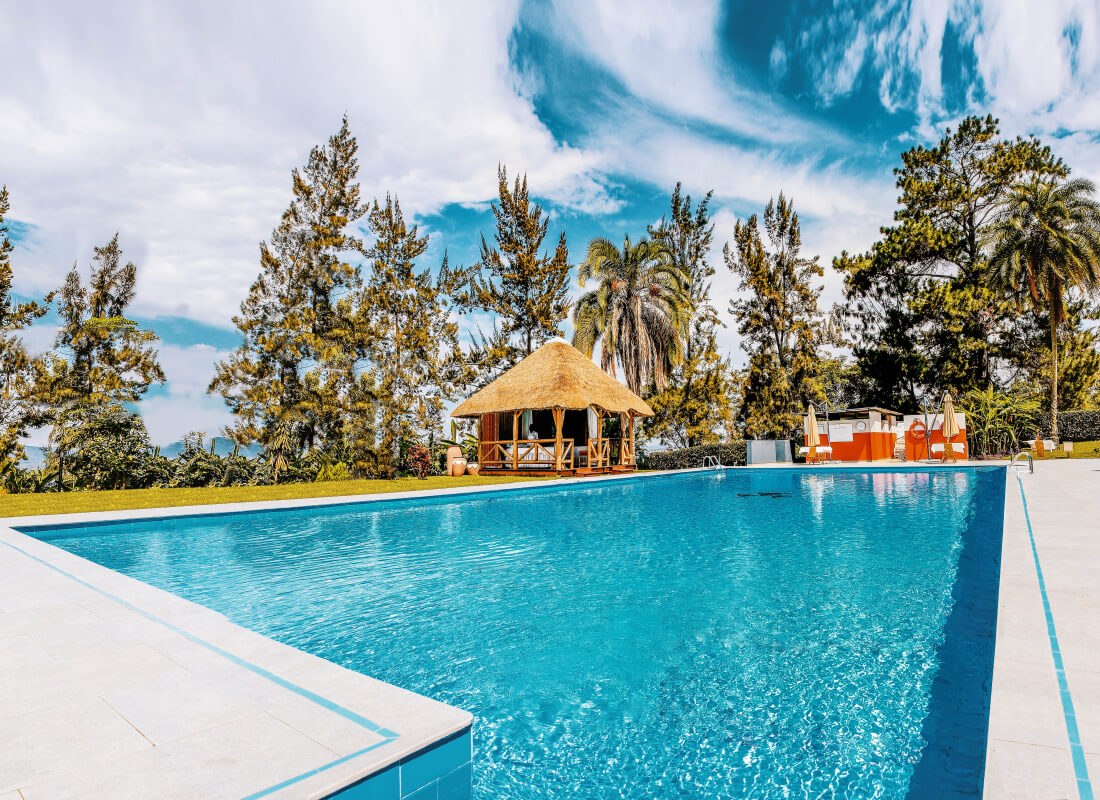 A swimming pool is overlooked by a thatch-roofed bar and trees. 