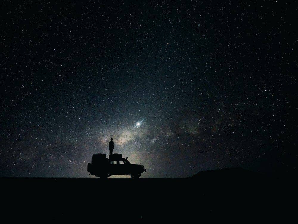 A man stands on a Jeep during a starry night in Namibia.