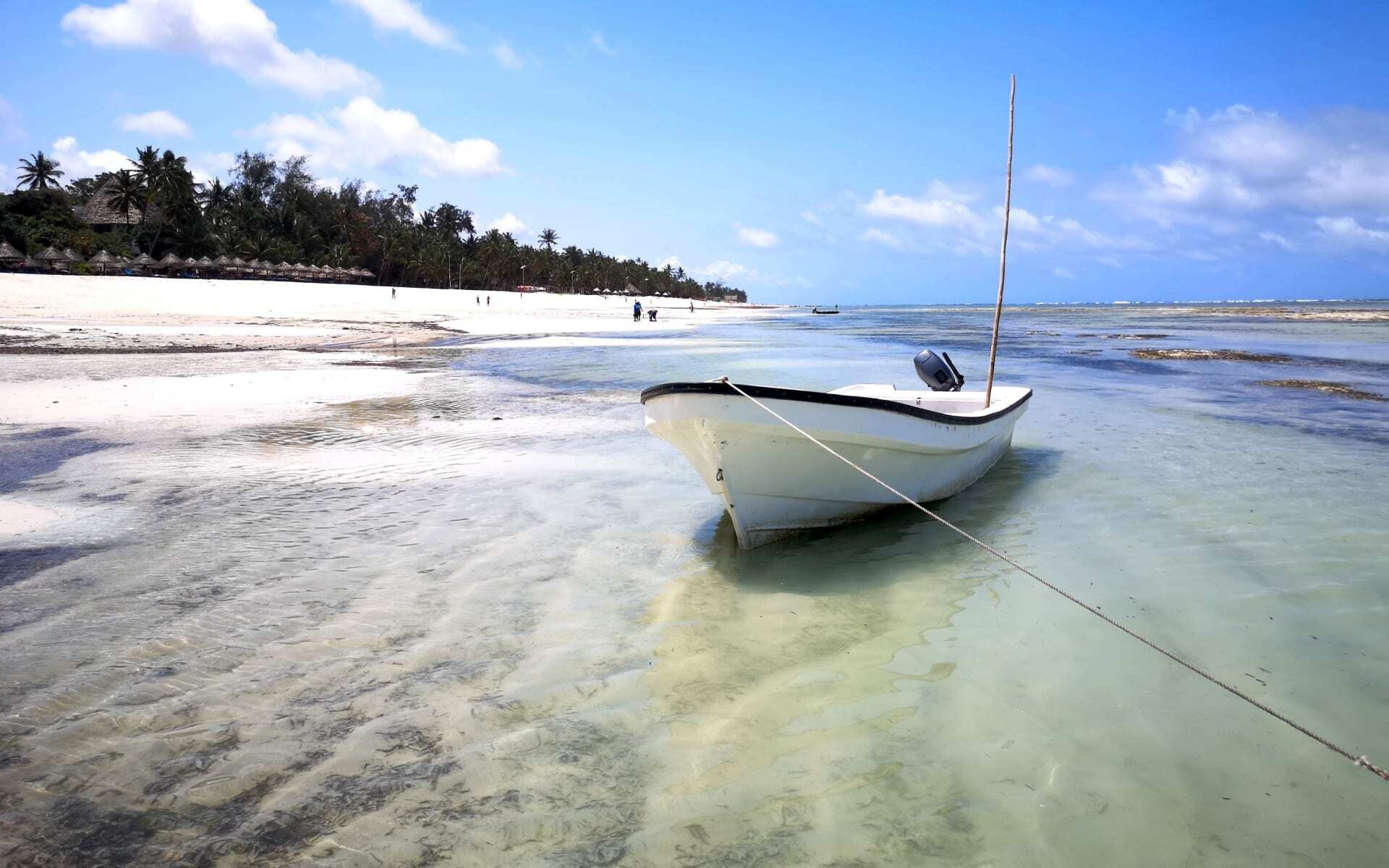 A boat sits on the shore of a white sanded beach in Kenya.
